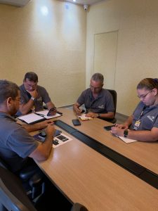 Foto da reunião de planejamento estratégico do Grupo Pinheiro com a presença de Marco Pinheiro, Thaynara, Cláudio, Max e Chrystian, discutindo ações de marketing e divulgação.